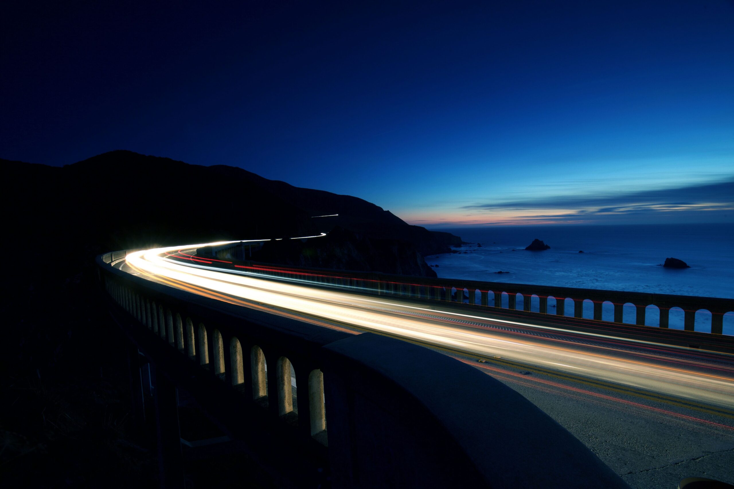 Cars speeding along a highway by the sea at night